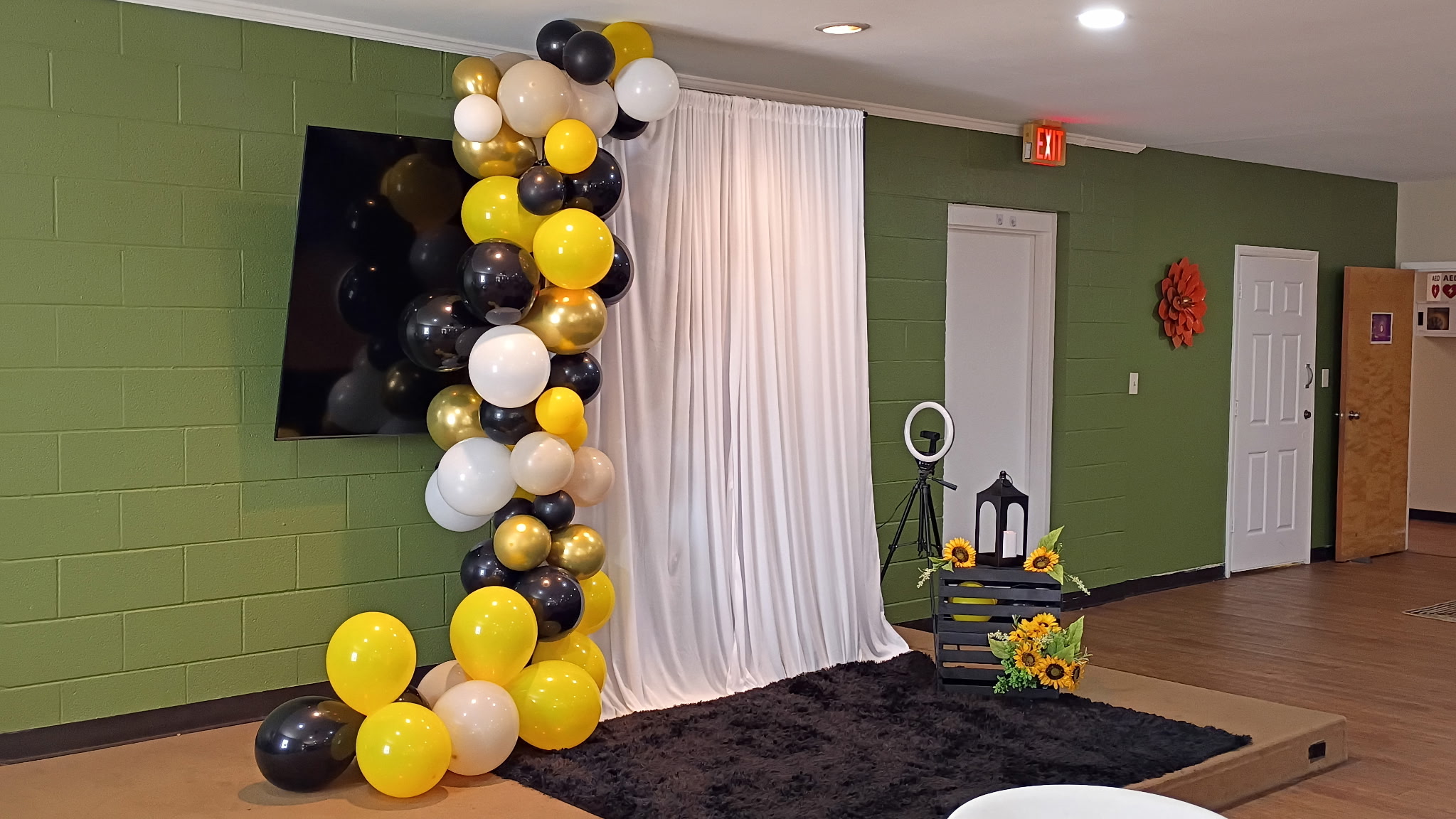 Black, gold, and white balloon photo area at a Bee's Tees Experience event